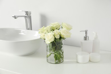 Bouquet of beautiful roses in vase and bath accessories near sink in bathroom