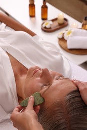 Photo of Woman receiving facial massage with jade gua sha tool in beauty salon, closeup