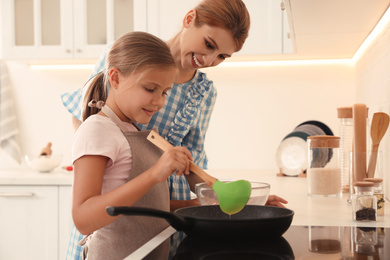 Mother and daughter making pancakes together in kitchen