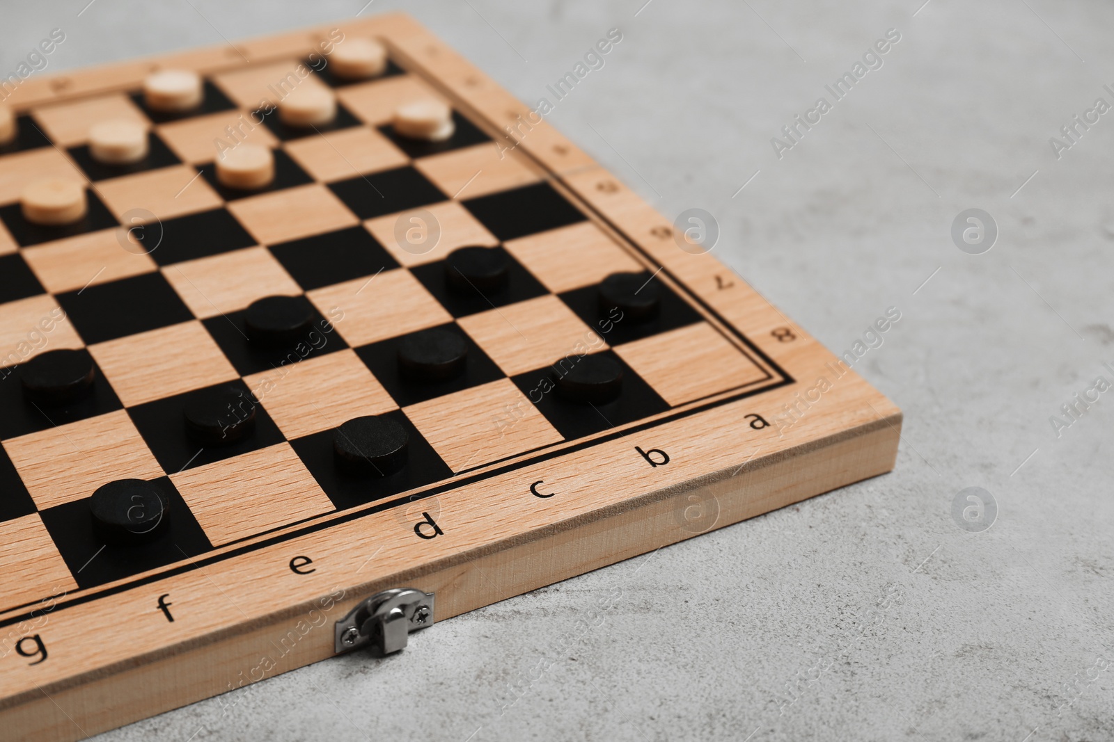 Photo of Wooden checkerboard with game pieces on light grey table, closeup