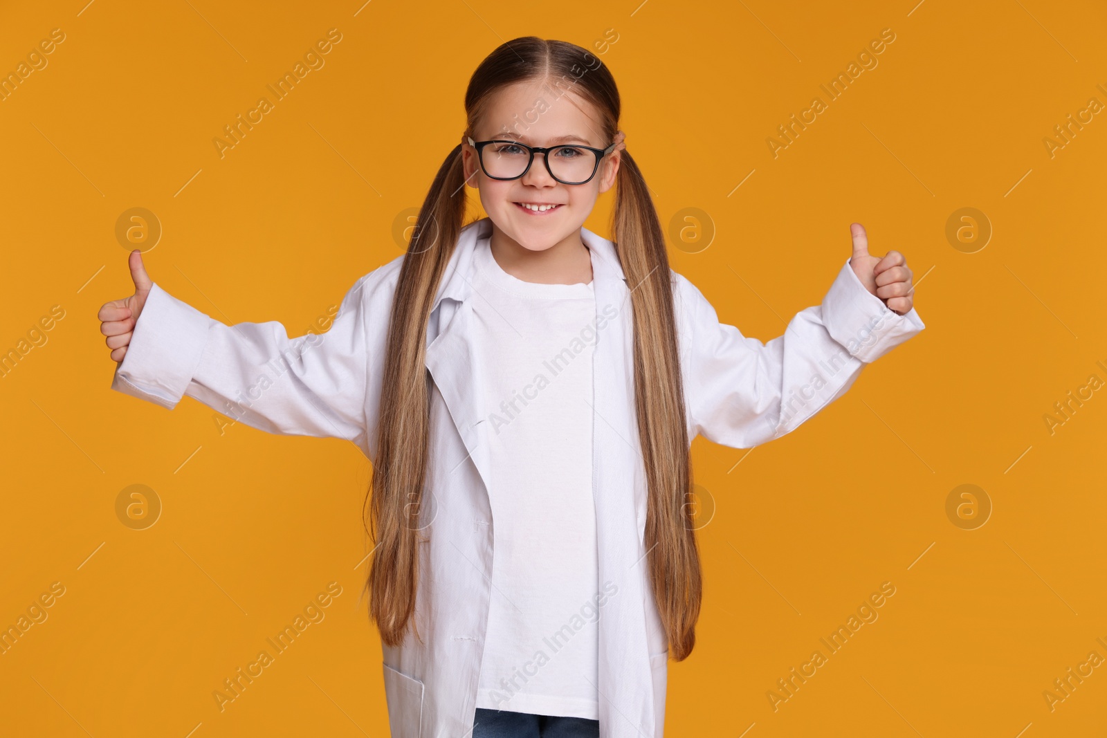 Photo of Little girl in medical uniform showing thumbs up on yellow background