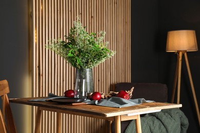 Set of clean dishware, ripe red apples and flowers on wooden table in stylish dining room