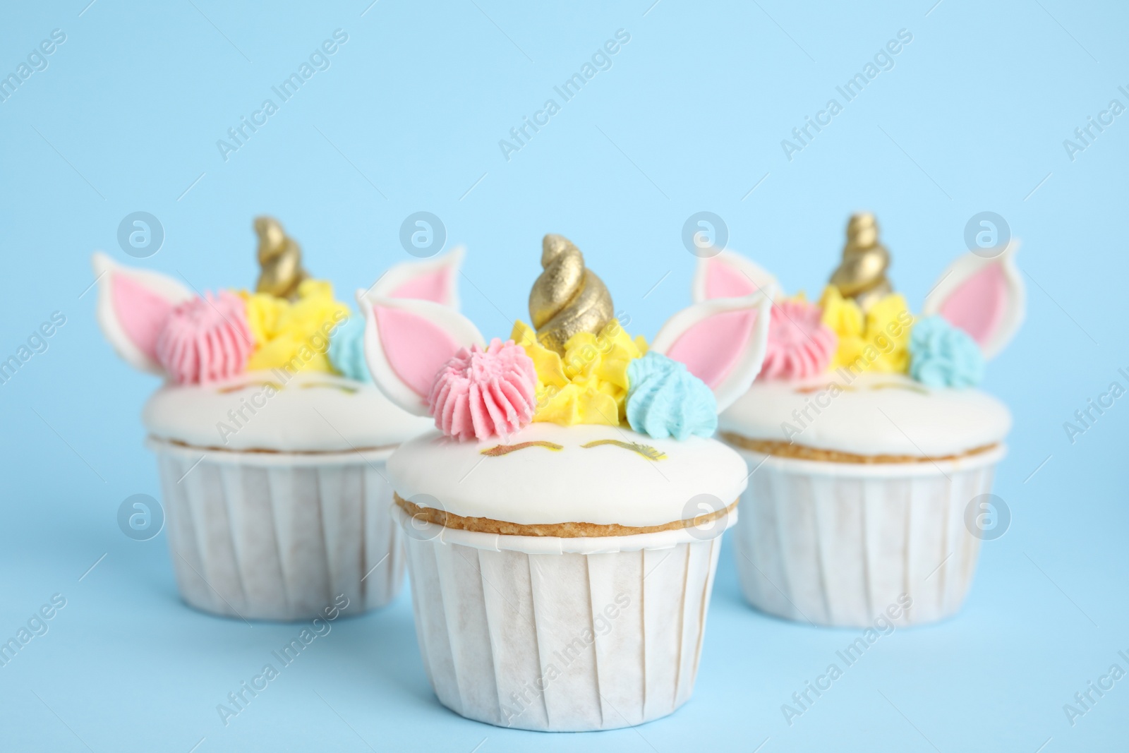 Photo of Cute sweet unicorn cupcakes on light blue background