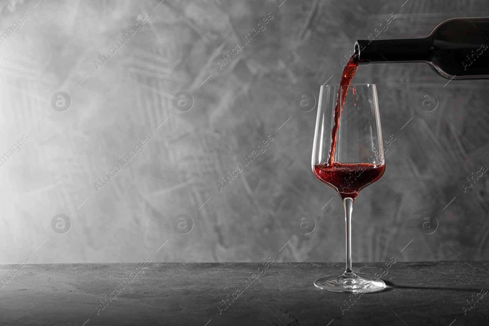 Photo of Pouring red wine from bottle into glass on table. Space for text