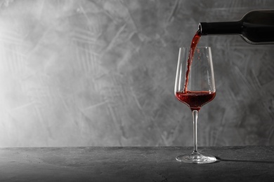 Photo of Pouring red wine from bottle into glass on table. Space for text