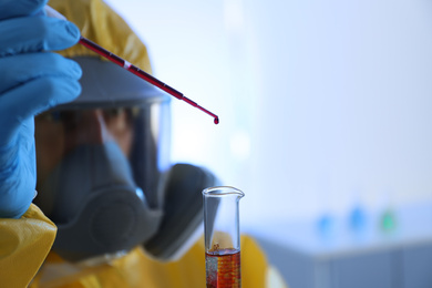 Scientist in chemical protective suit dripping blood  into test tube, focus on laboratory glassware. Virus research