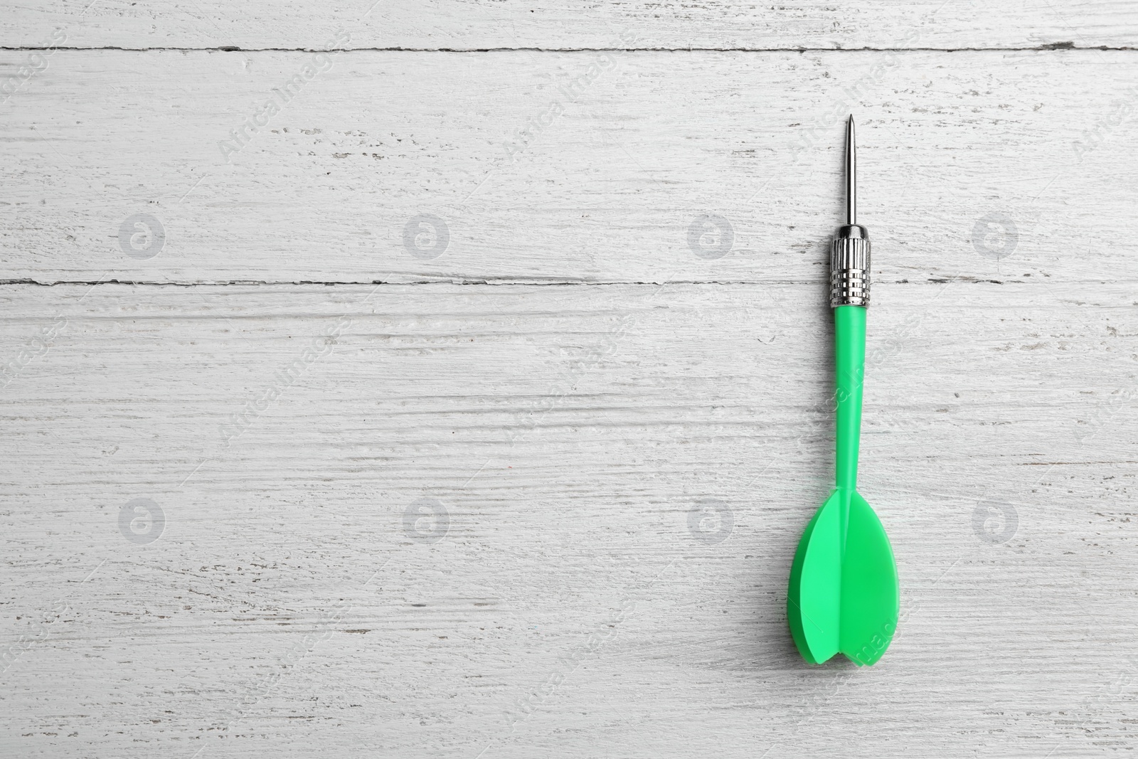 Photo of Green dart arrow on white wooden table, top view with space for text