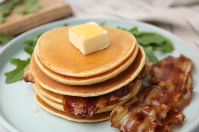 Tasty pancakes with butter, fried bacon and fresh arugula on white marble table, closeup