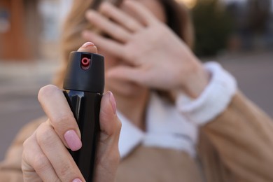 Photo of Young woman covering eyes with hand and using pepper spray outdoors