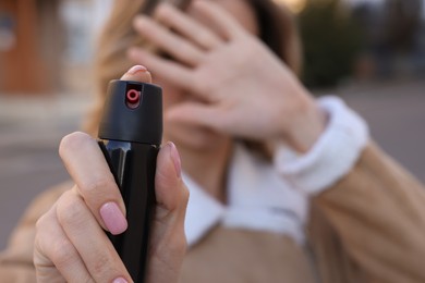 Young woman covering eyes with hand and using pepper spray outdoors