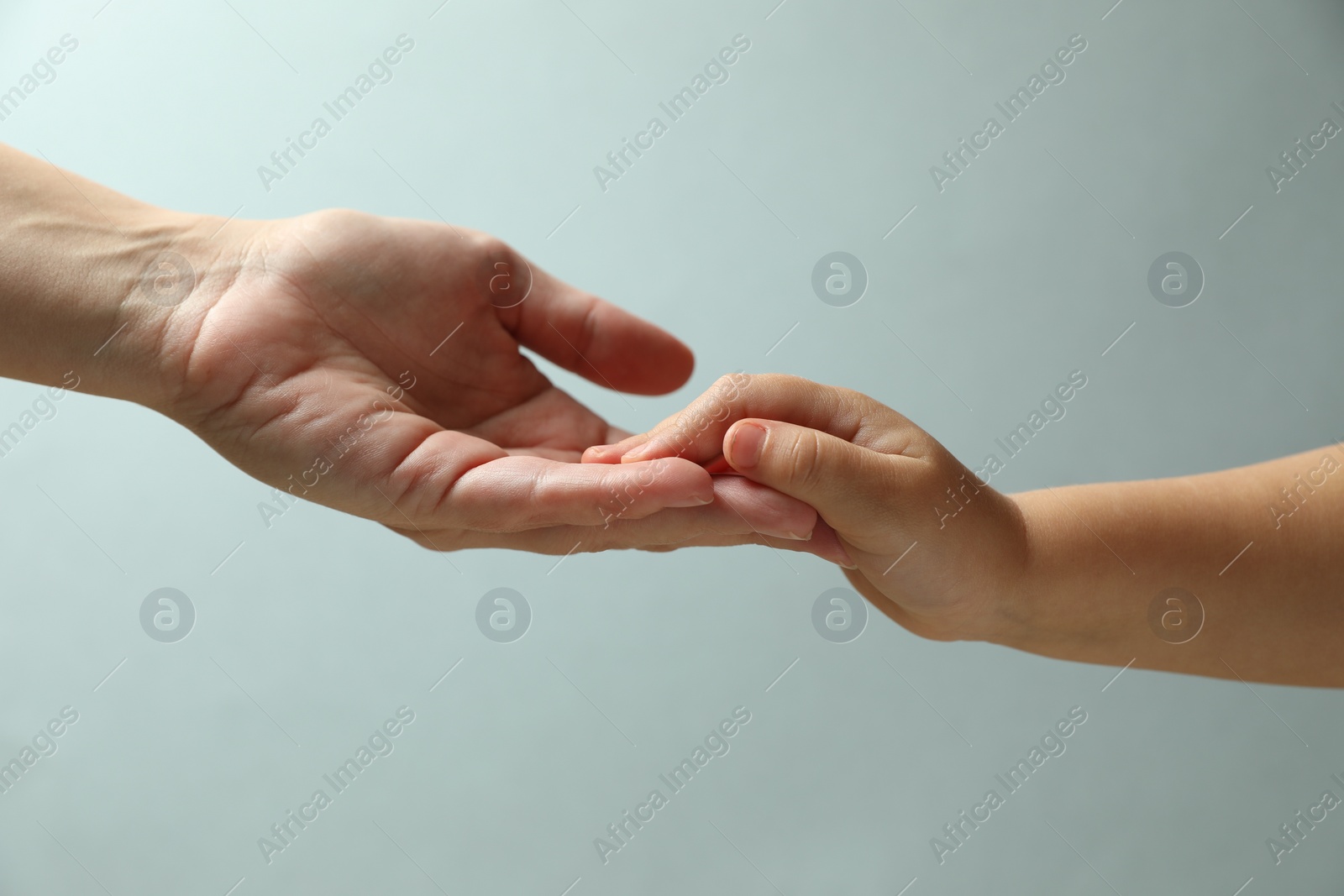 Photo of Mother and child holding hands on light blue background, closeup