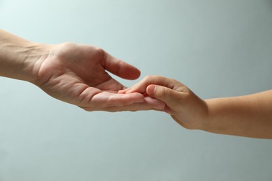 Mother and child holding hands on light blue background, closeup