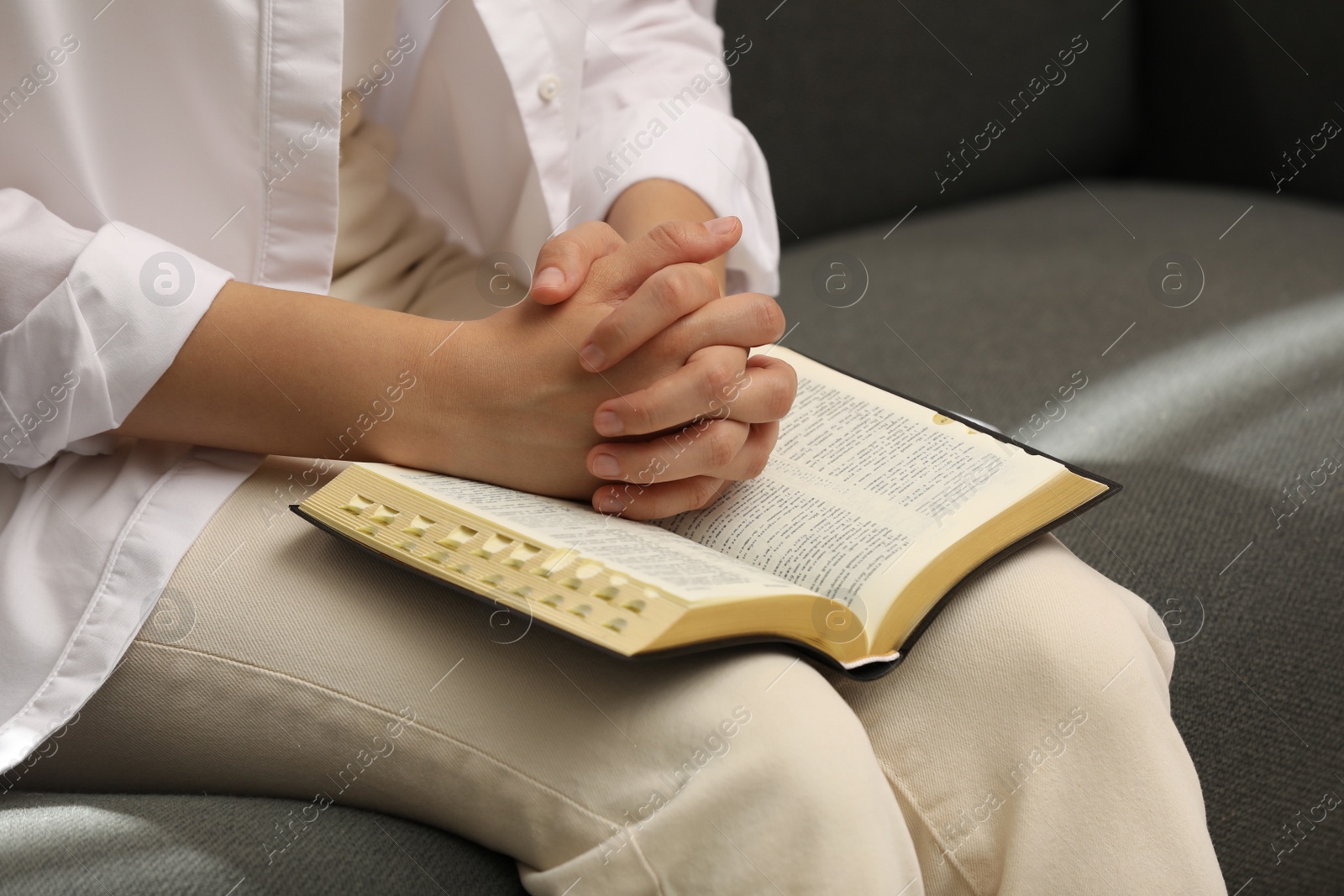 Photo of Religious woman praying over Bible indoors, closeup