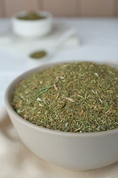 Dried dill in bowl on white wooden table, closeup