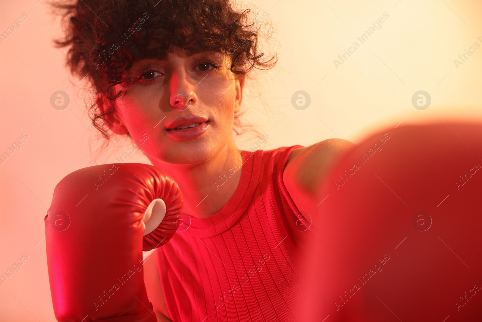 Photo of Beautiful young woman with boxing gloves on color background in neon lights, closeup