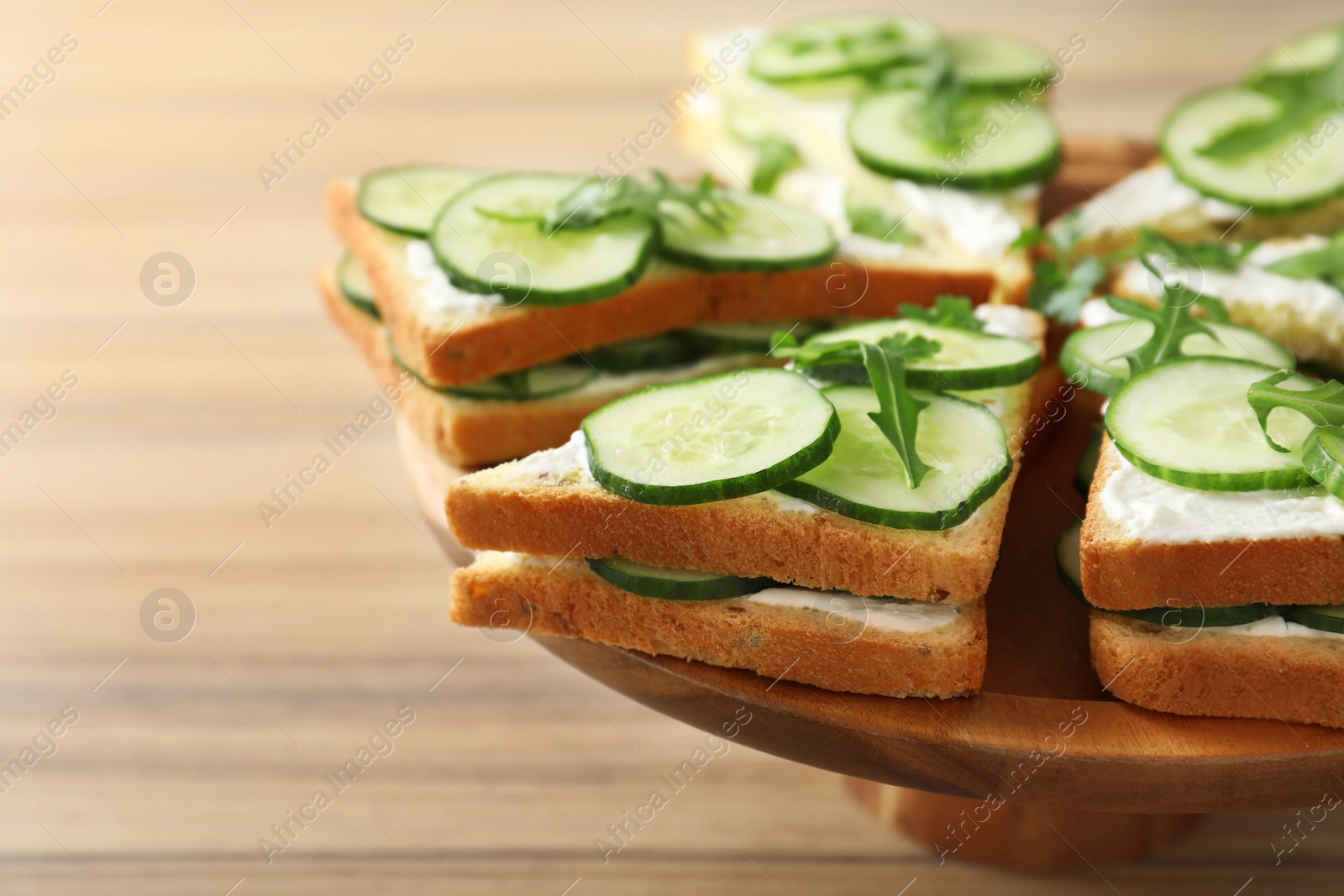 Photo of Wooden stand with traditional English cucumber sandwiches on table, closeup