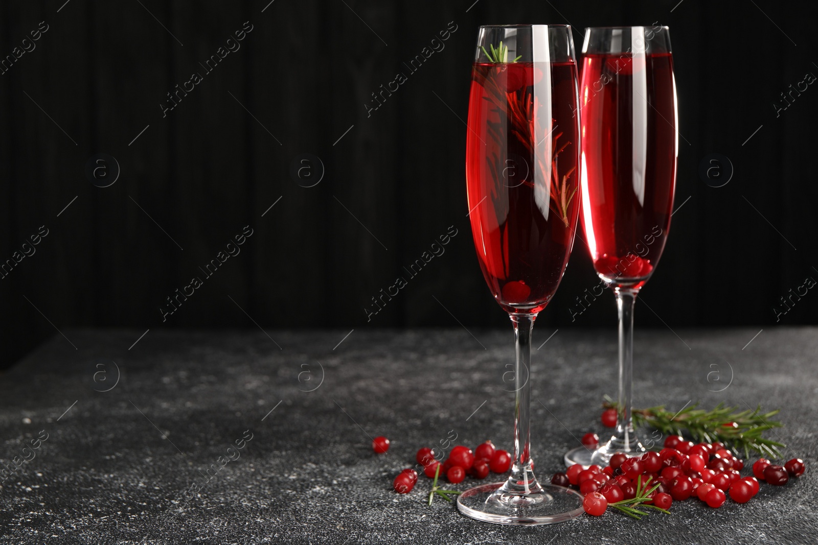 Photo of Tasty cranberry cocktail with rosemary in glasses on gray textured table against dark background, space for text
