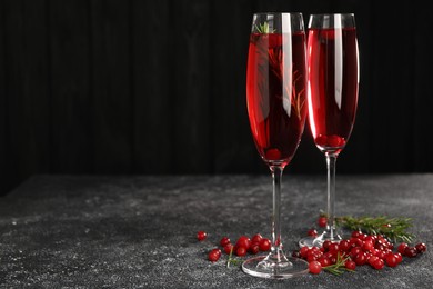 Photo of Tasty cranberry cocktail with rosemary in glasses on gray textured table against dark background, space for text