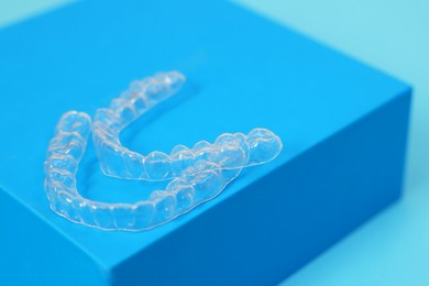 Photo of Transparent dental aligners on light blue background, closeup. Space for text