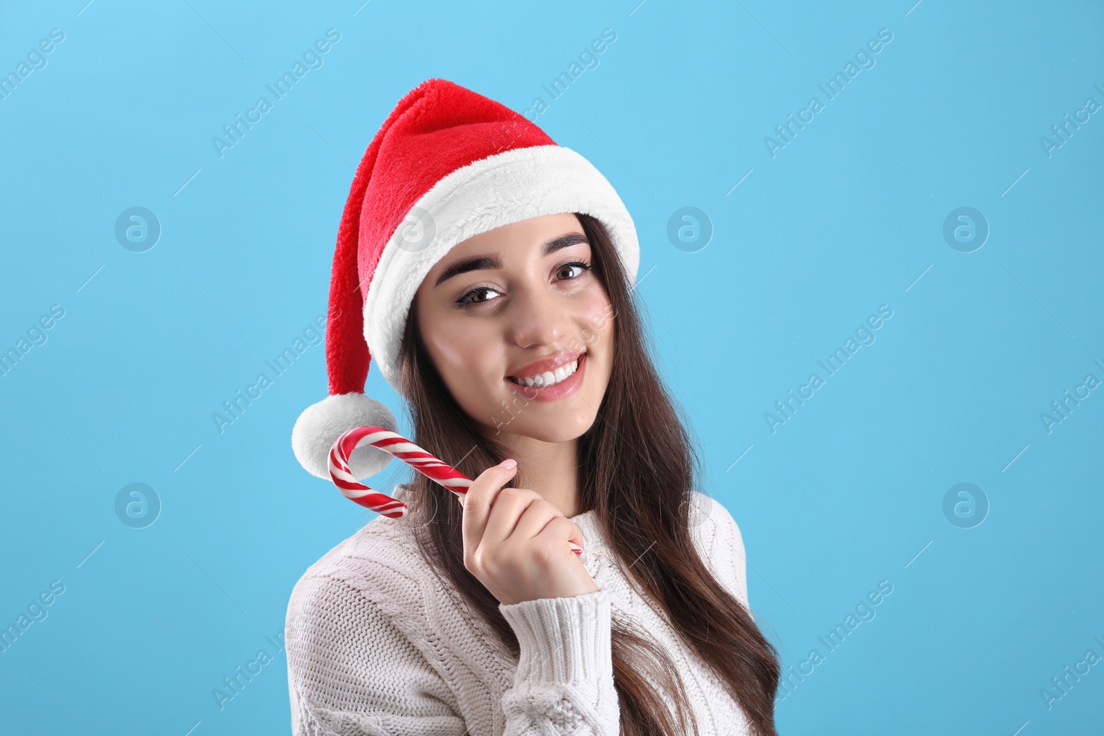 Photo of Beautiful woman in Santa Claus hat holding candy cane on light blue background