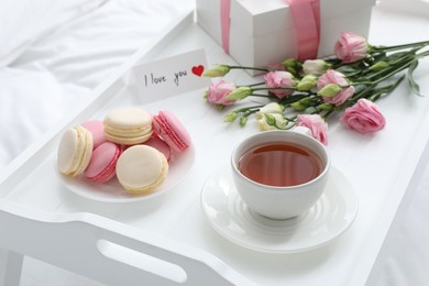 Photo of Tasty breakfast served in bed. Delicious macarons, tea, gift box, flowers and I Love You card on tray