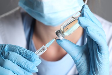 Doctor filling syringe with medication from glass vial, closeup