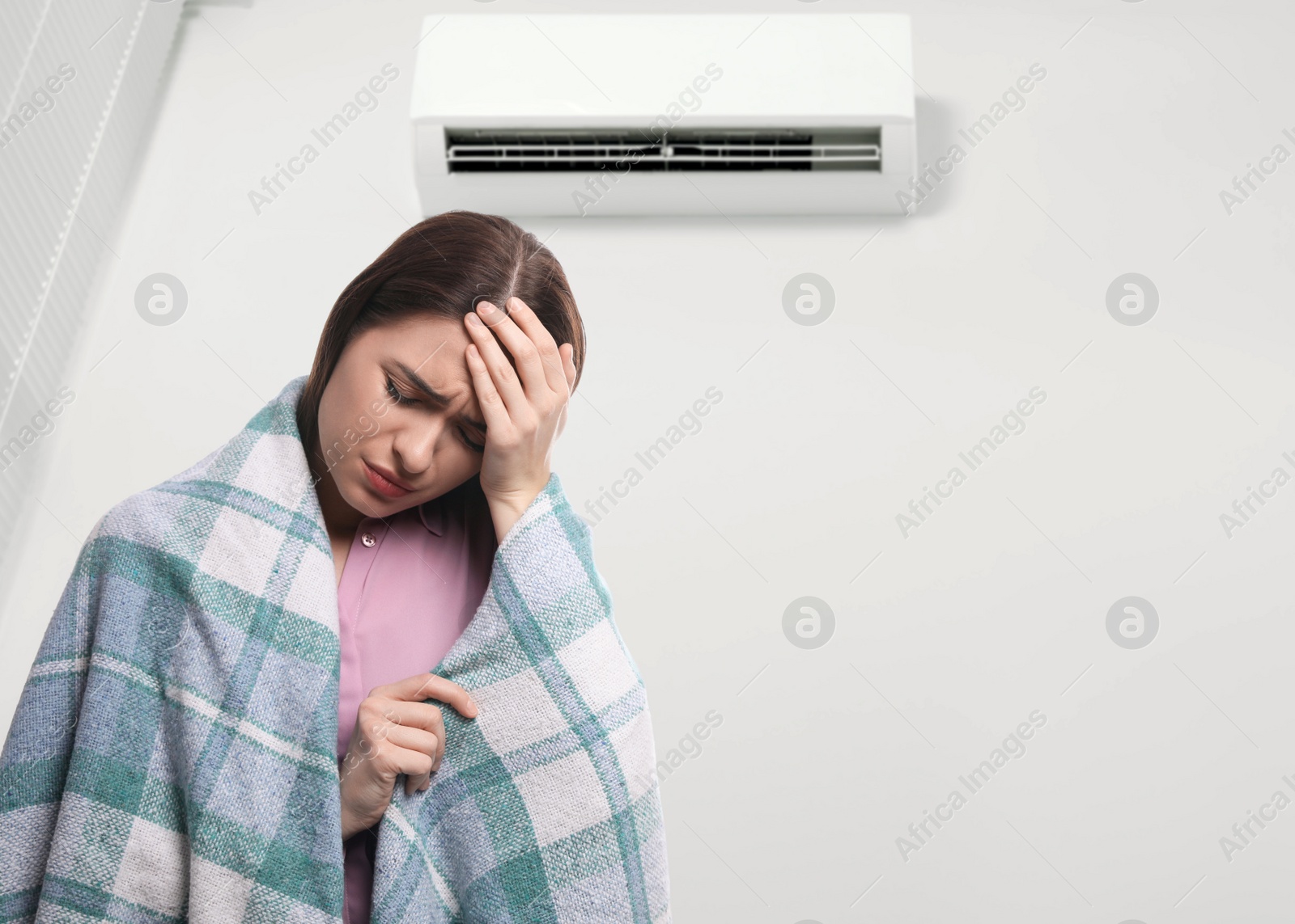 Image of Woman suffering from cold in room with air conditioner on white wall, space for text