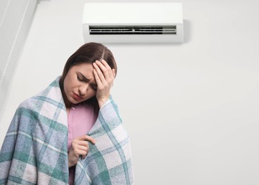 Woman suffering from cold in room with air conditioner on white wall, space for text