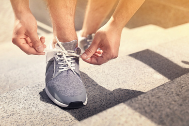 Image of Young man tying shoelaces on his sneakers outdoors on sunny day, closeup