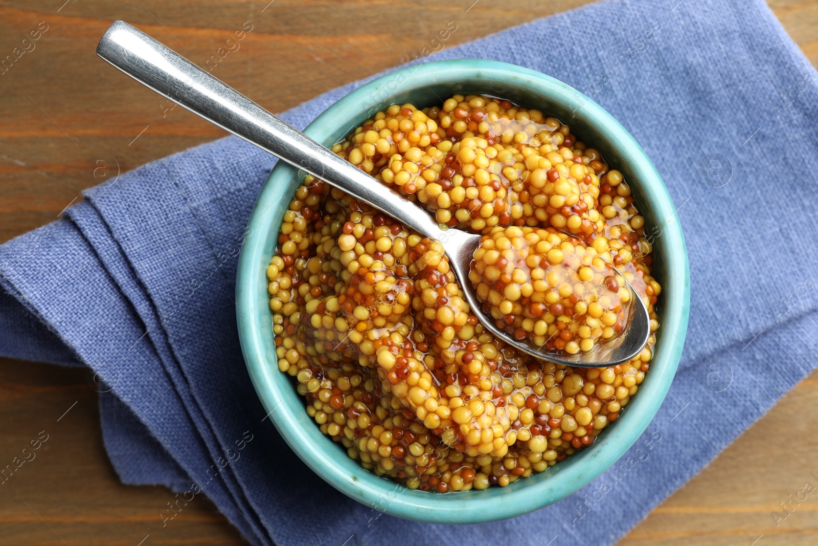 Photo of Whole grain mustard in bowl and spoon on wooden table, top view