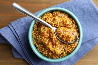 Whole grain mustard in bowl and spoon on wooden table, top view