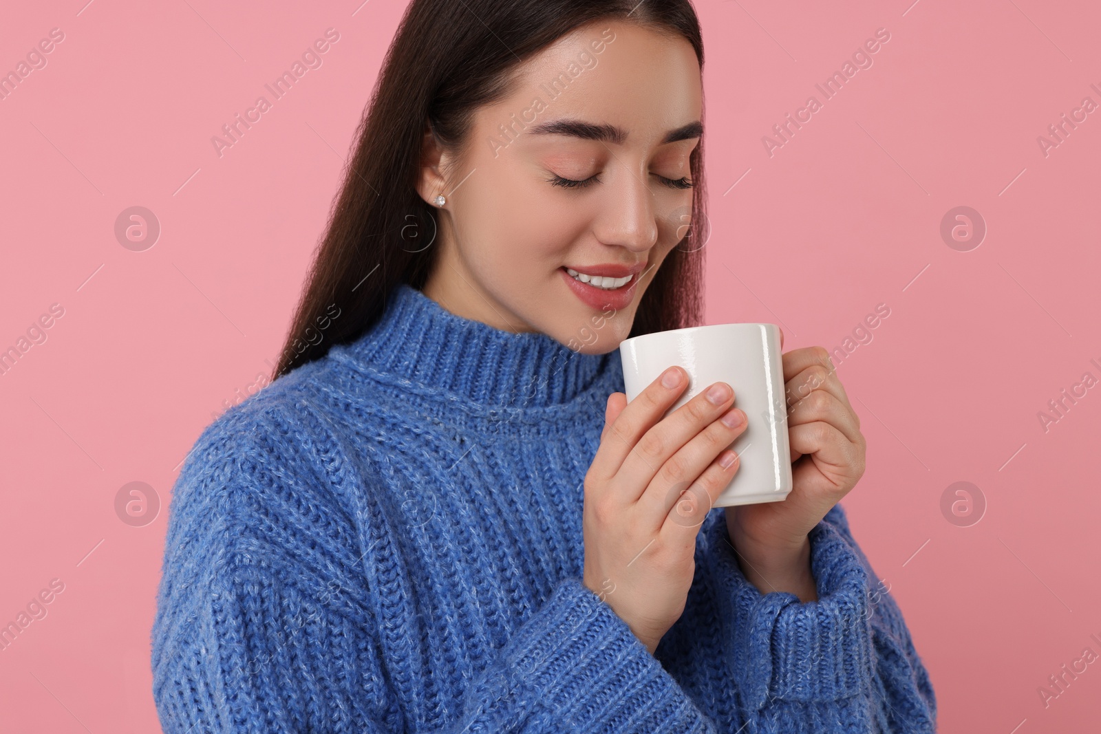 Photo of Happy young woman holding white ceramic mug on pink background