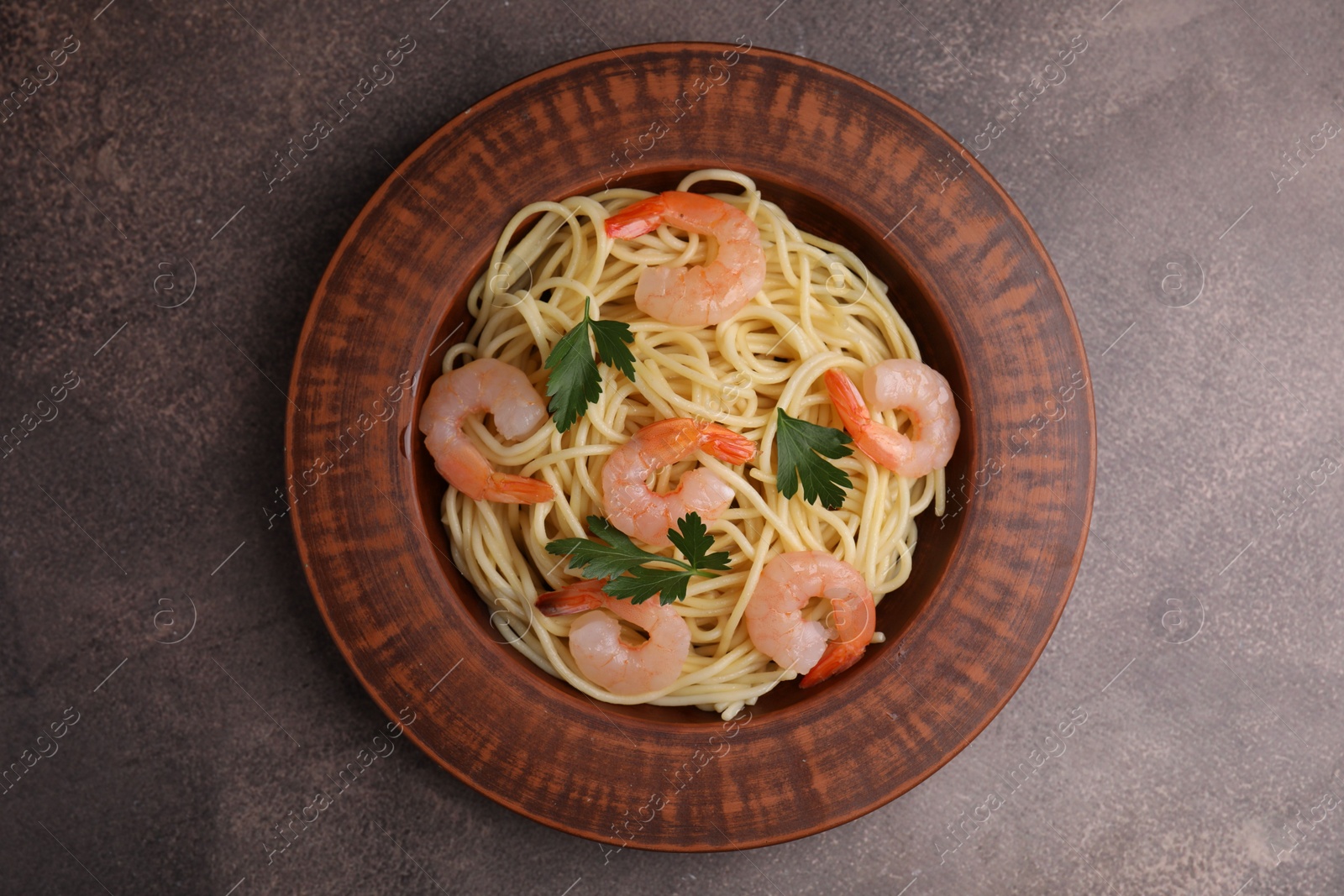 Photo of Tasty spaghetti with shrimps and parsley on brown textured table, top view