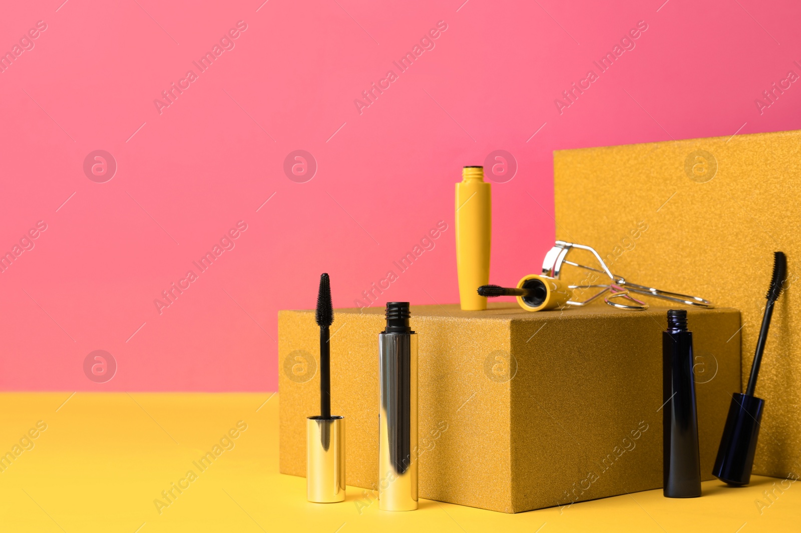 Photo of Different mascaras and eyelash curler on yellow background, space for text. Makeup product