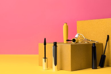 Photo of Different mascaras and eyelash curler on yellow background, space for text. Makeup product