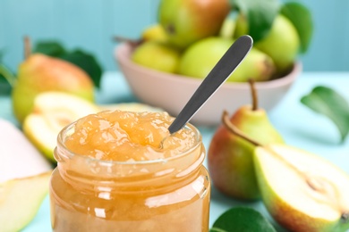 Photo of Tasty homemade pear jam and fresh fruits on light blue table, closeup