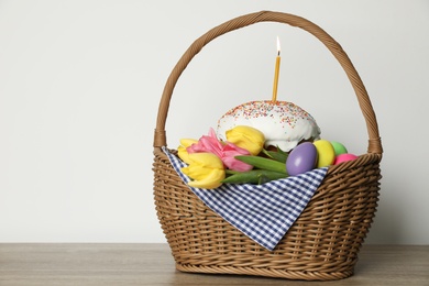 Traditional Easter cake with burning candle, dyed eggs and flowers in basket on table against white background. Space for text