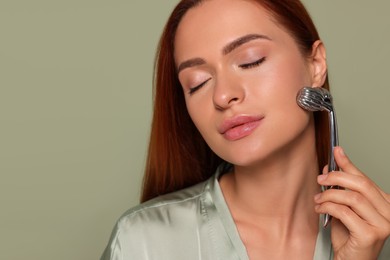 Photo of Young woman massaging her face with metal roller on green background, closeup. Space for text