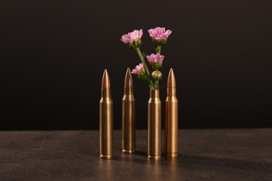 Photo of Bullets and cartridge case with beautiful flowers on grey table against dark background