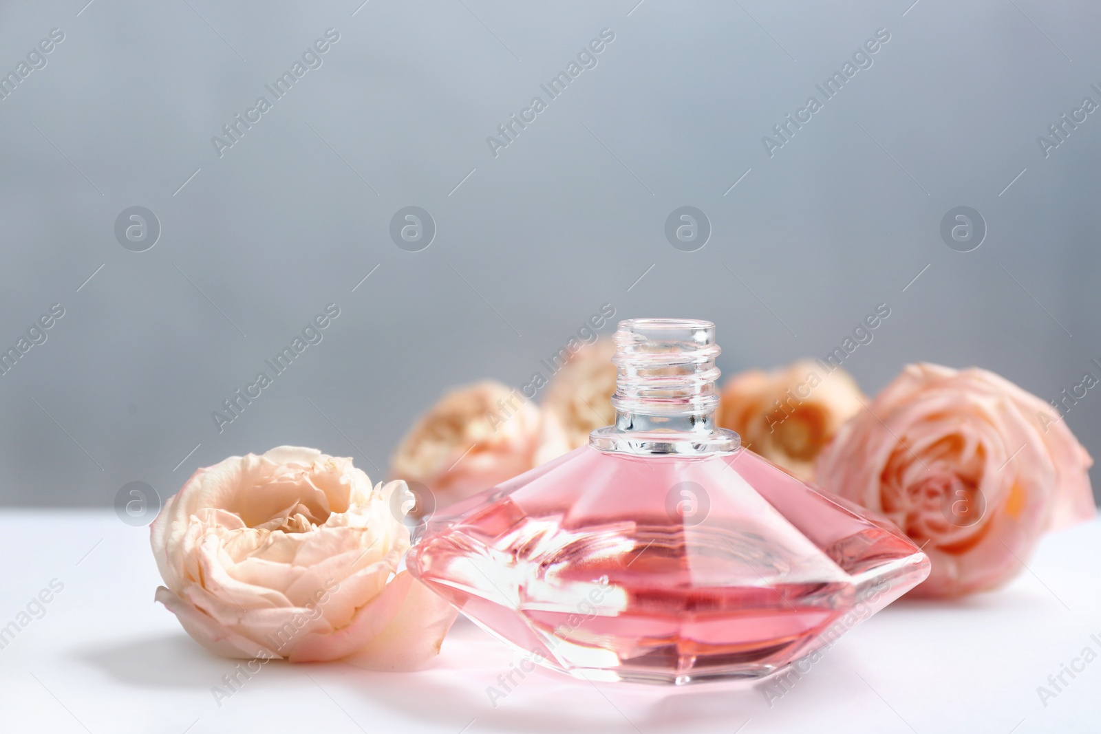 Photo of Bottle of perfume with beautiful roses on table