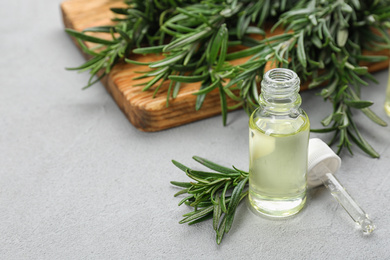 Photo of Fresh rosemary and bottle of essential oil on light grey table. Space or text