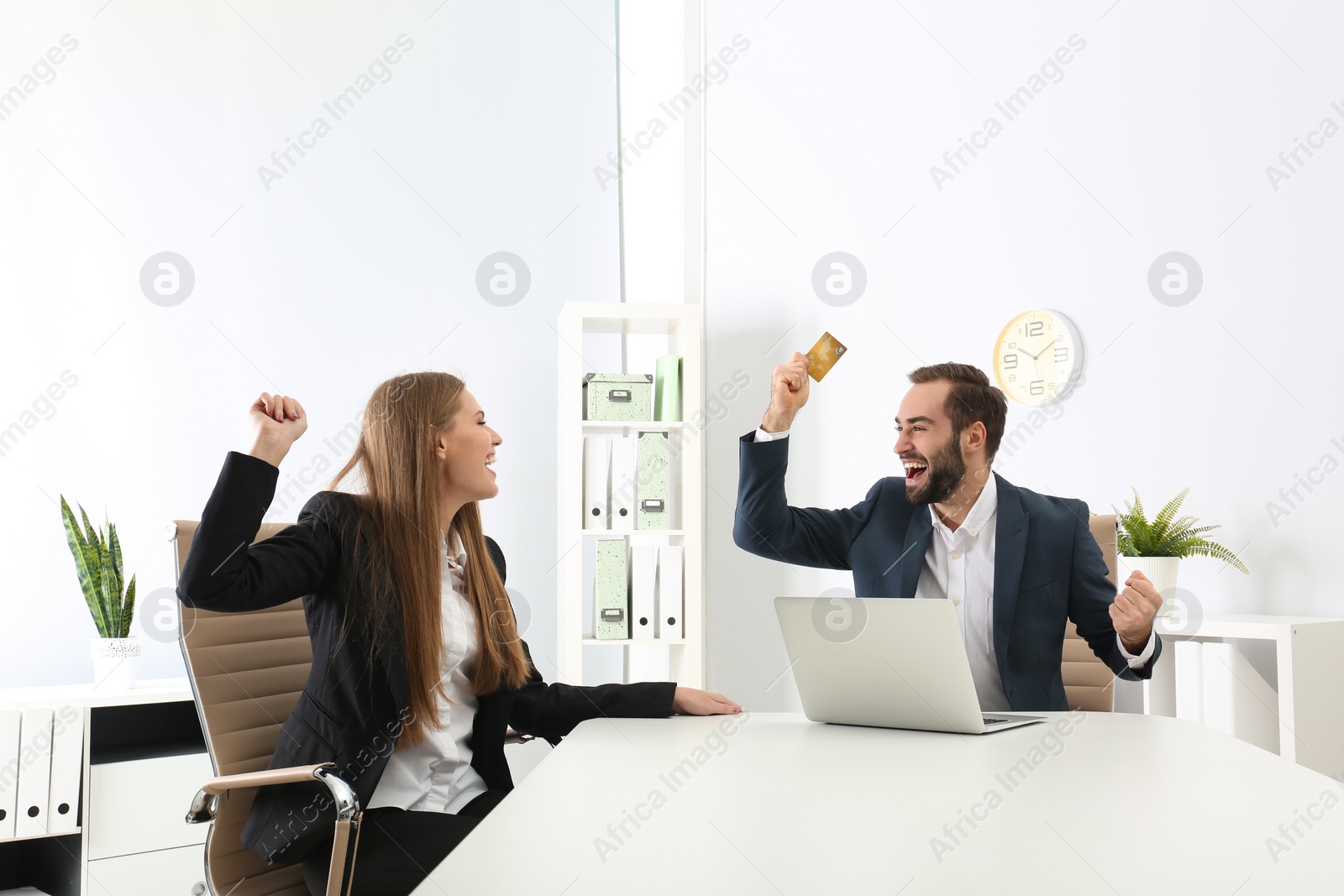 Photo of Emotional young people with credit card and laptop celebrating victory in office