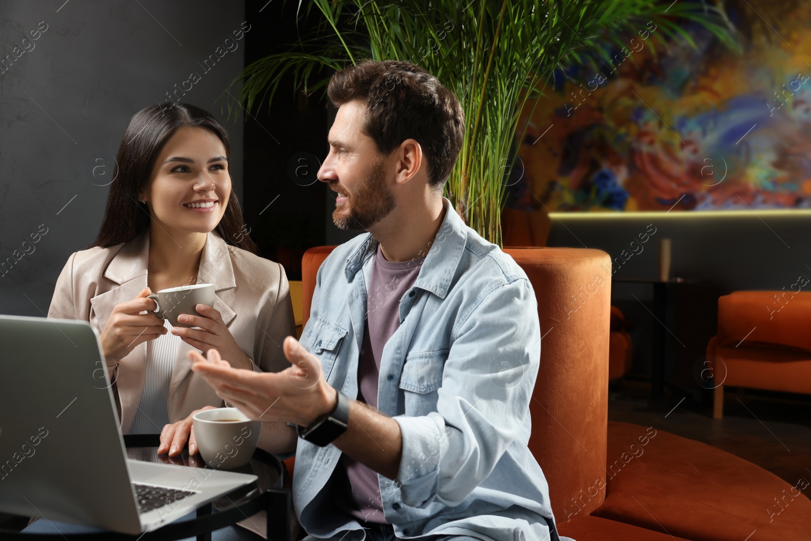 Photo of Couple with coffee and laptop spending time together in cafe