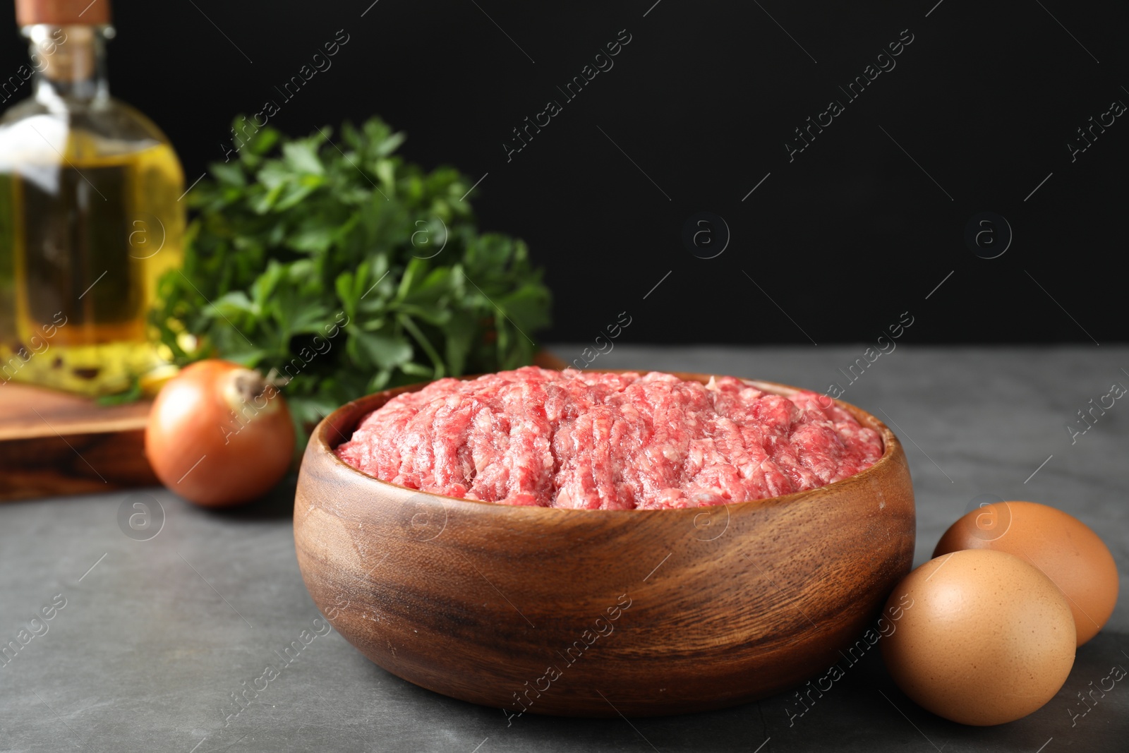 Photo of Raw ground meat in bowl and different products on grey table