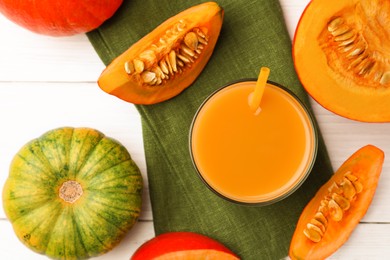 Tasty pumpkin juice in glass and different pumpkins on white wooden table, flat lay
