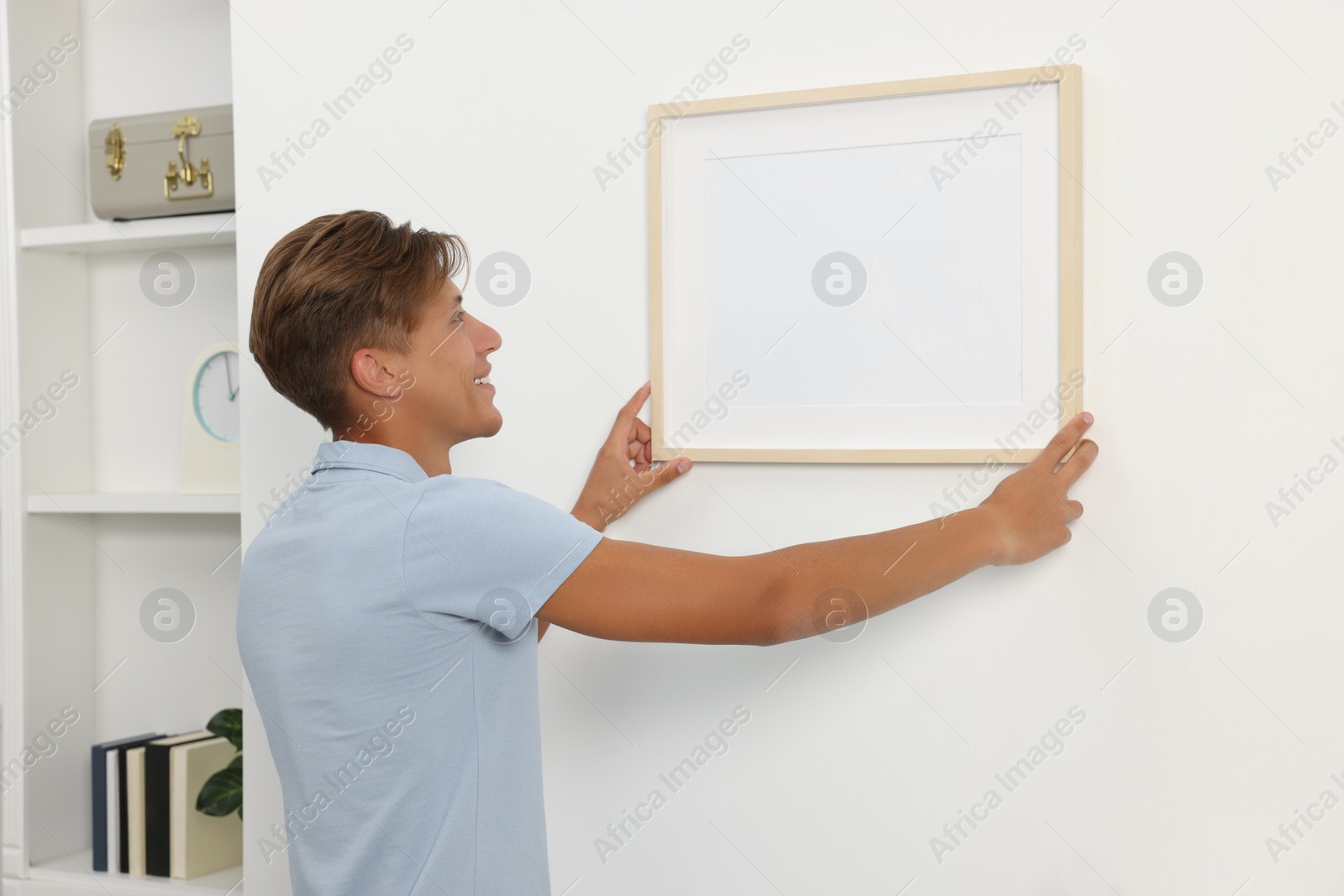 Photo of Young man hanging picture frame on white wall indoors