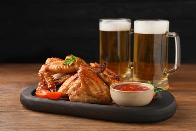 Mugs with beer, delicious baked chicken wings and sauce on wooden table