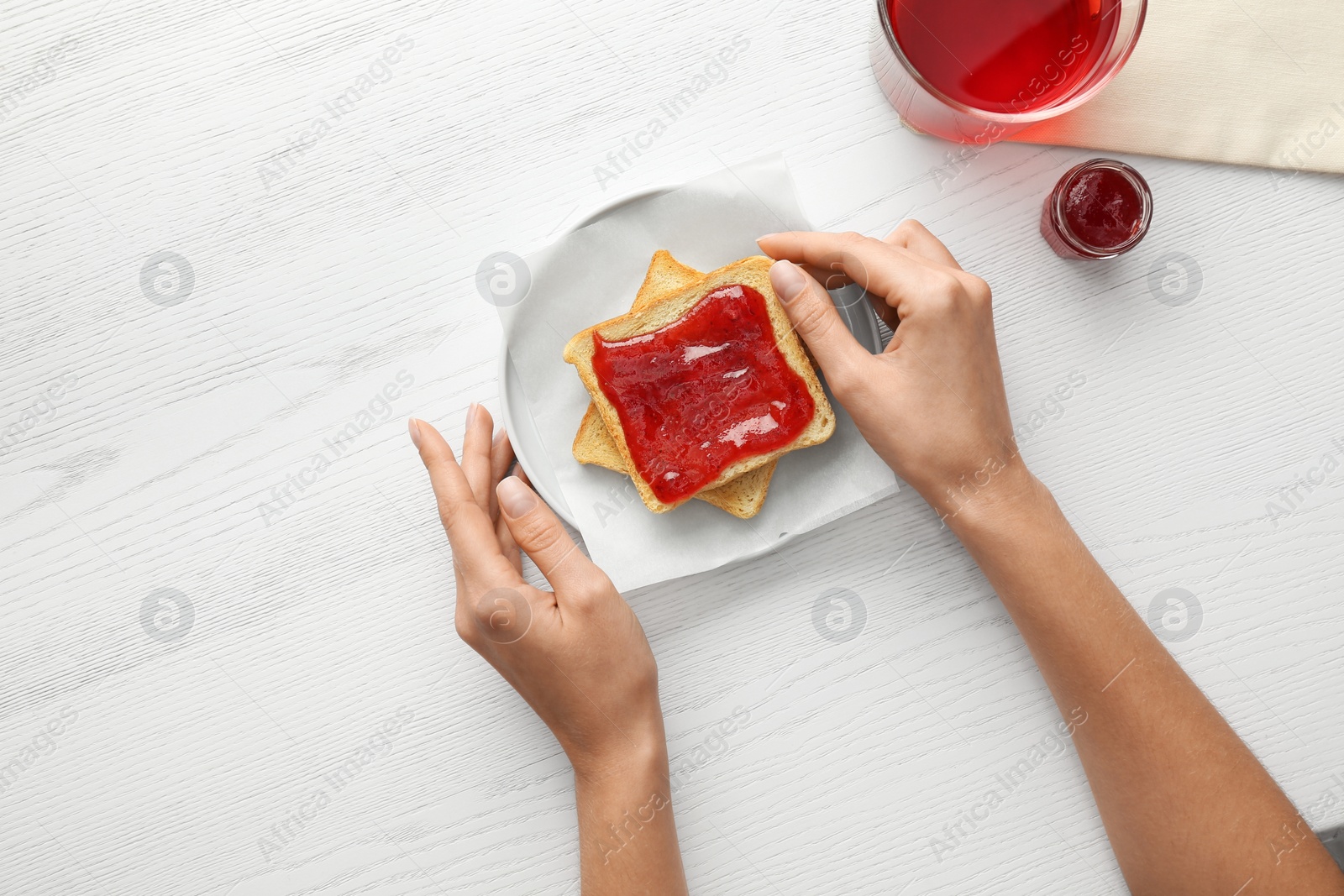 Photo of Woman eating toast with jam at white wooden table, top view. Delicious morning meal