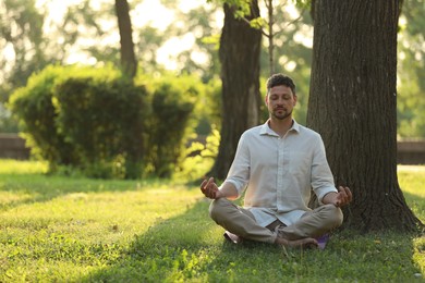 Photo of Man meditating in park on sunny summer day. Space for text
