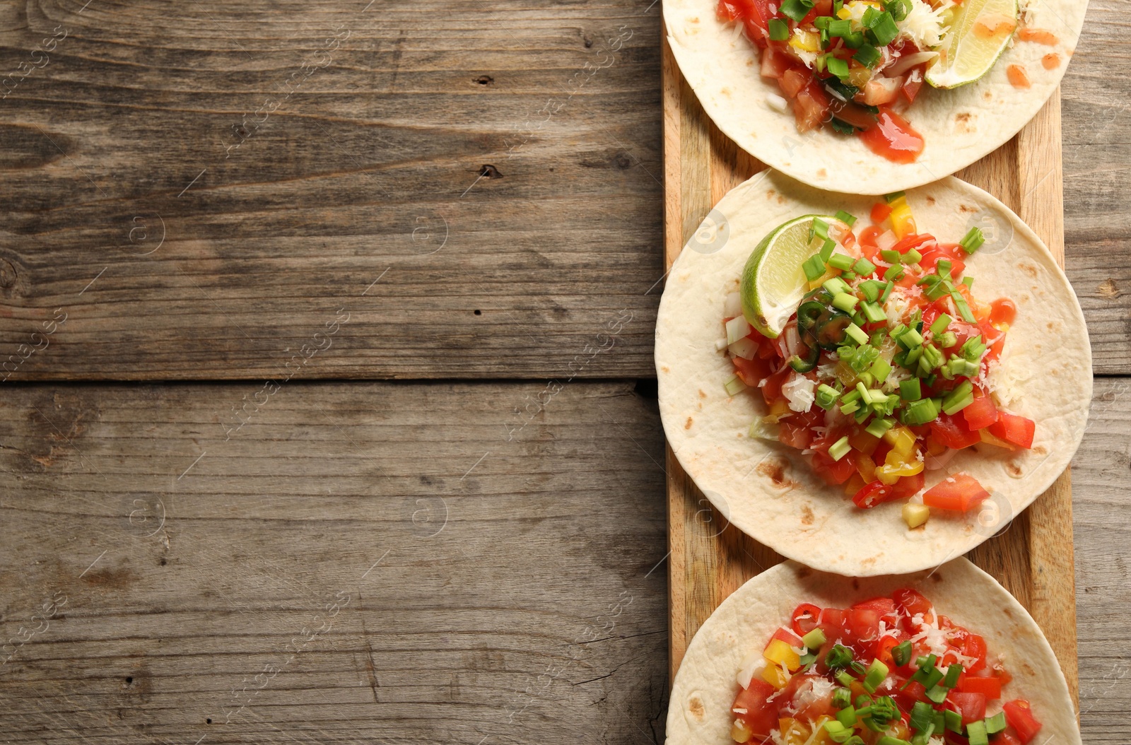 Photo of Delicious tacos with vegetables, green onion, lime and ketchup on wooden table, top view. Space for text